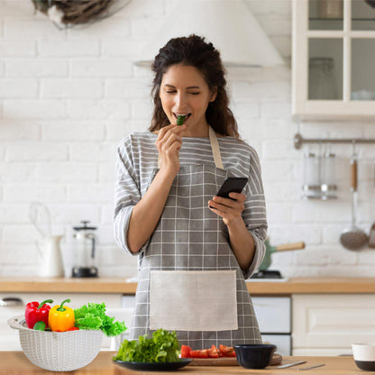 Woman in a kitchen eating a green leafy vegetable and looking at her phone.